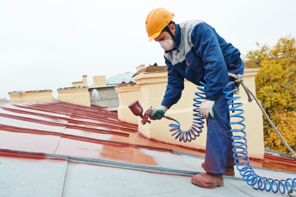 A man in hard hat painting a roof with pulveriser spraying paint